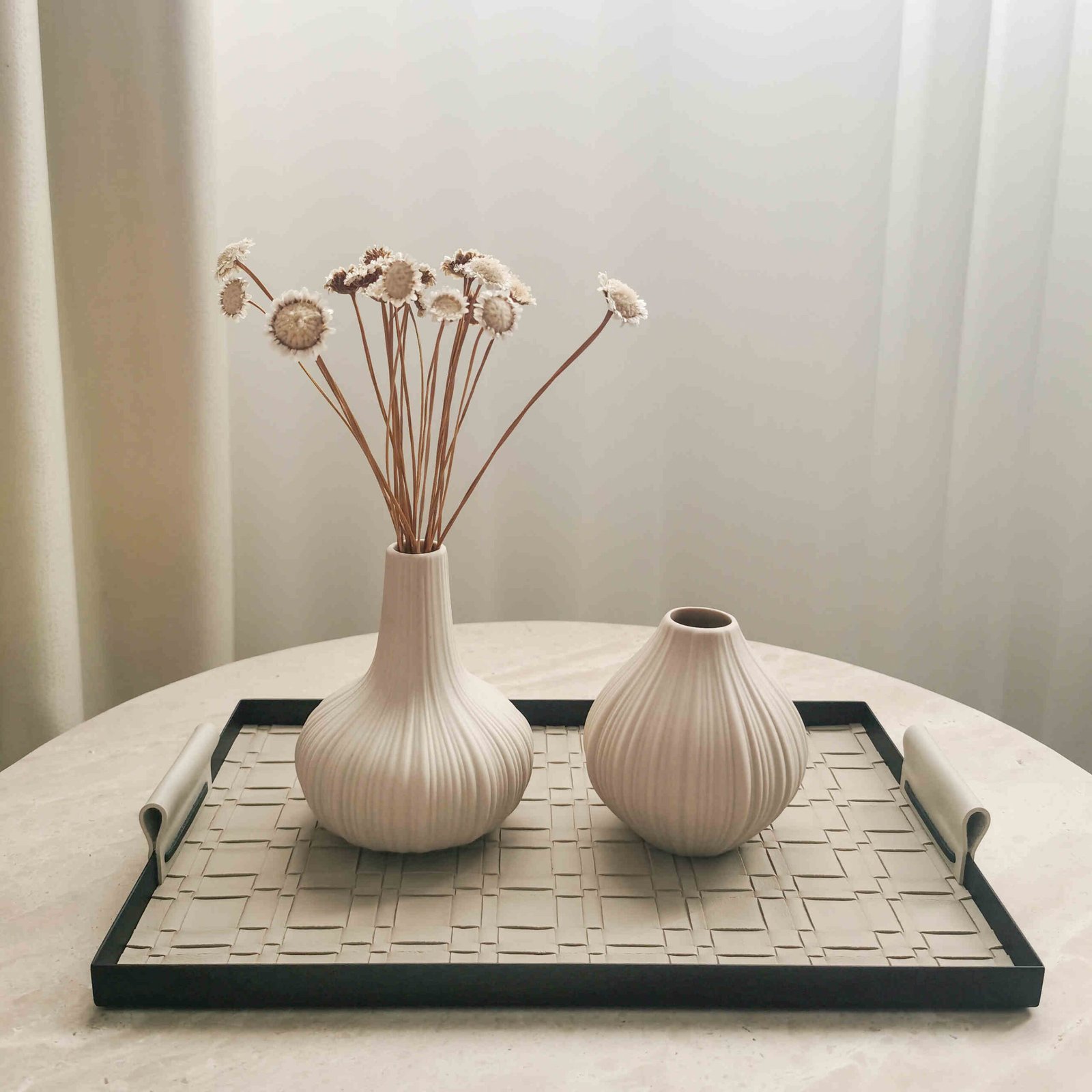 Two beige ceramic vases styled with dried stems on a tray